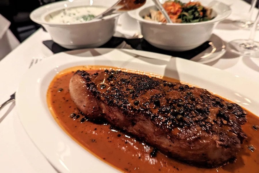 Steak au poivre on a white plate with two white bowls of sides in the background.