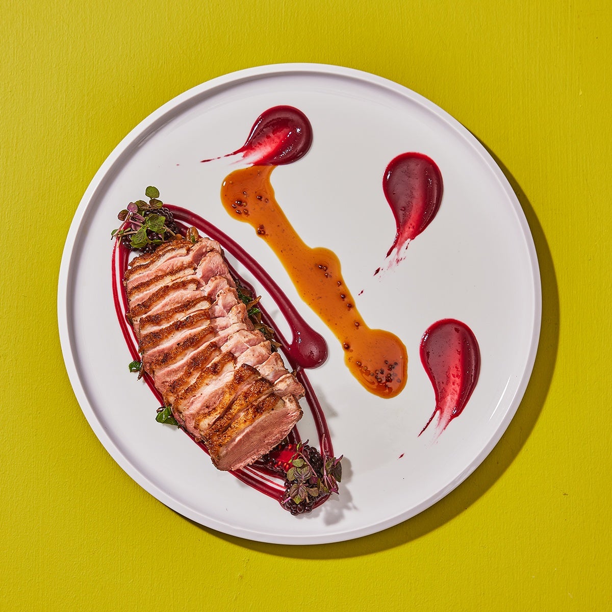 A colorful plate of seared duck breast from French restaurant Deuxave against a green-yellow background.