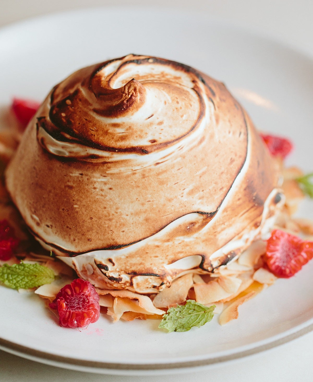 A small meringue dessert garnished with cut up raspberries and leaves.