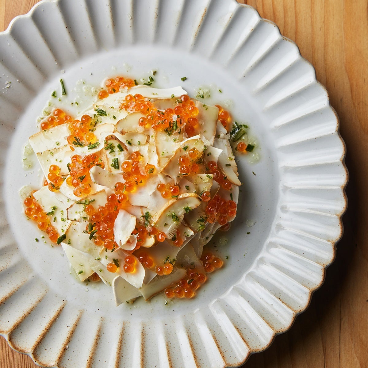 A white plate of orange trout roe and green rosemary flakes sprinkled over black butter–celery root purée, lightly colored mushrooms.