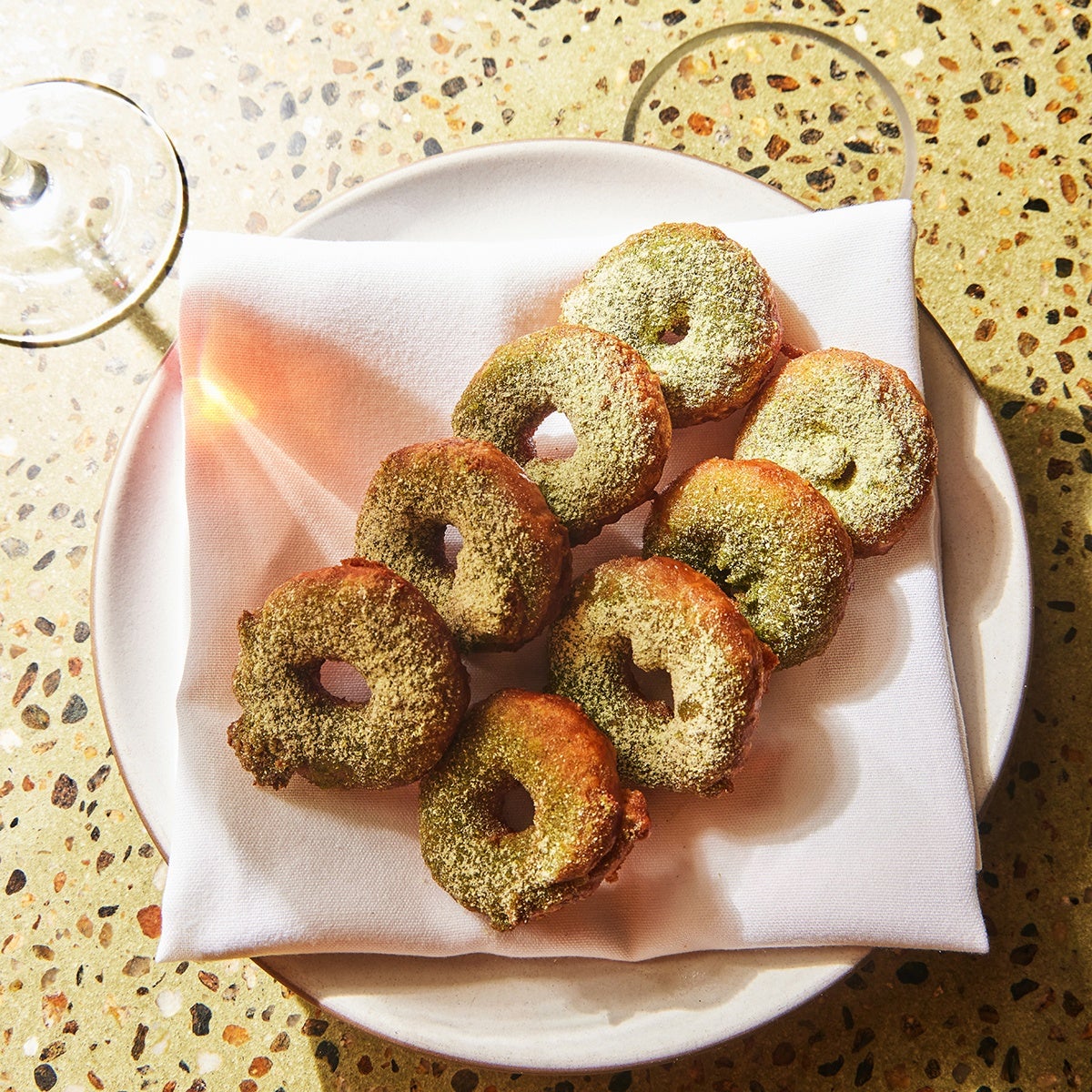 Eight sunchoke doughnuts with XO Gouda and powdered leeks, laid evenly on a white-cloth napkin that's on a plate.