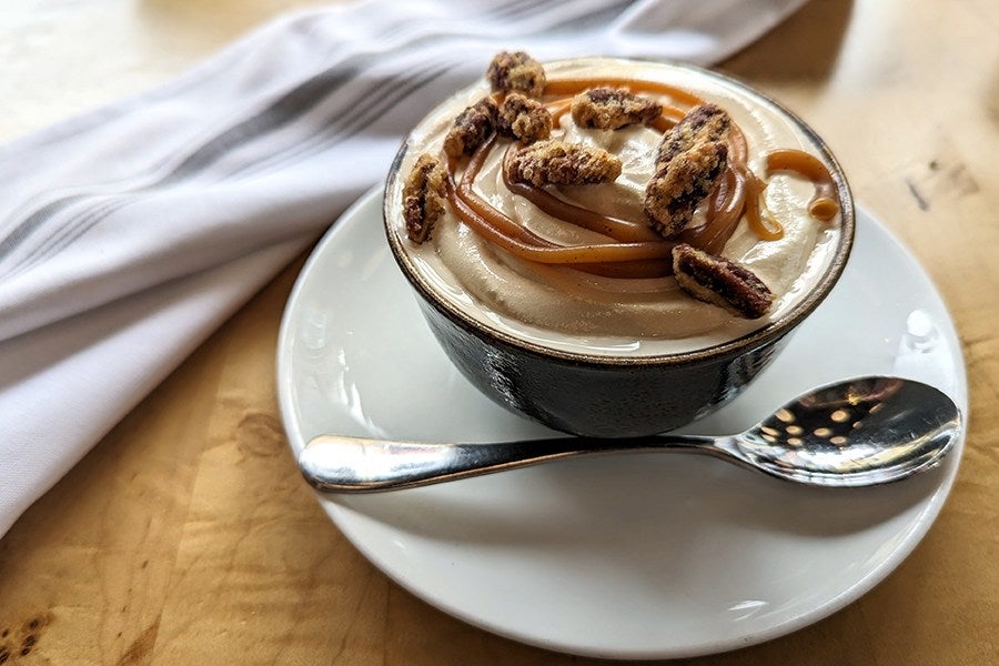 A bowl of melty soft serve ice cream topped with a swirl of caramel and candied nuts.