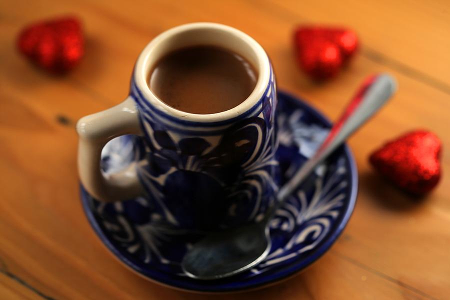 A small white and blue mug is filled with a thick drinking chocolate and sits on a wooden table.