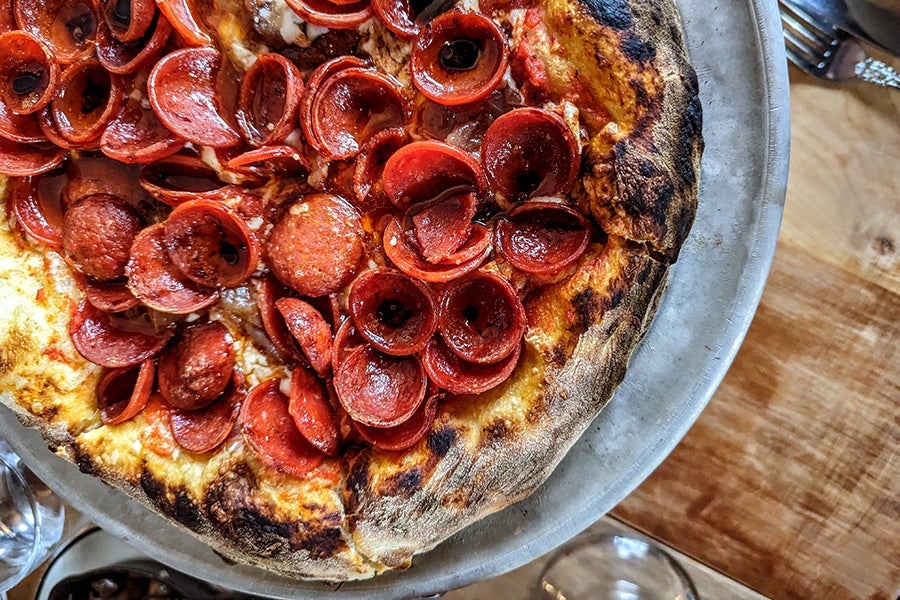 Overhead view of a very pepperoni-covered pizza with a slightly charred crust.