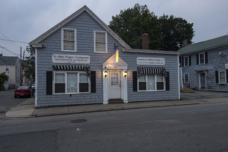 Exterior view of a small gray house with signage that says Ye Olde Pepper Companie Manufacturing Confectioner Since 1806. Another sign identifies it as America's Oldest Candy Co.
