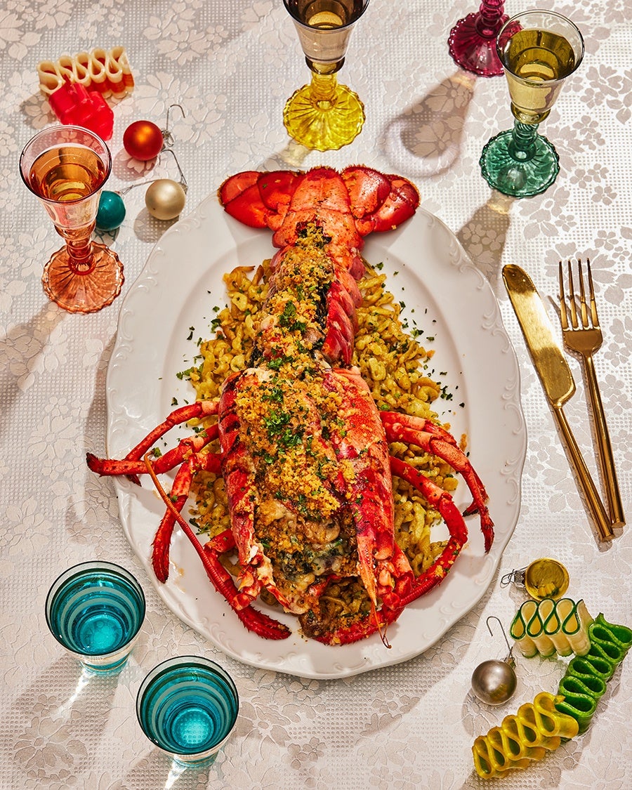 Overhead view of an elaborate stuffed lobster dish on a white platter, surrounded by colorful glassware and holiday ornaments.