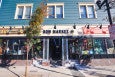 Exterior of a building, with retail spaces on the first floor. Signage reads Blue Bandana Relics, Bow Market, and Tiny Turns Paperie, and a breezeway is built through the center of the building.