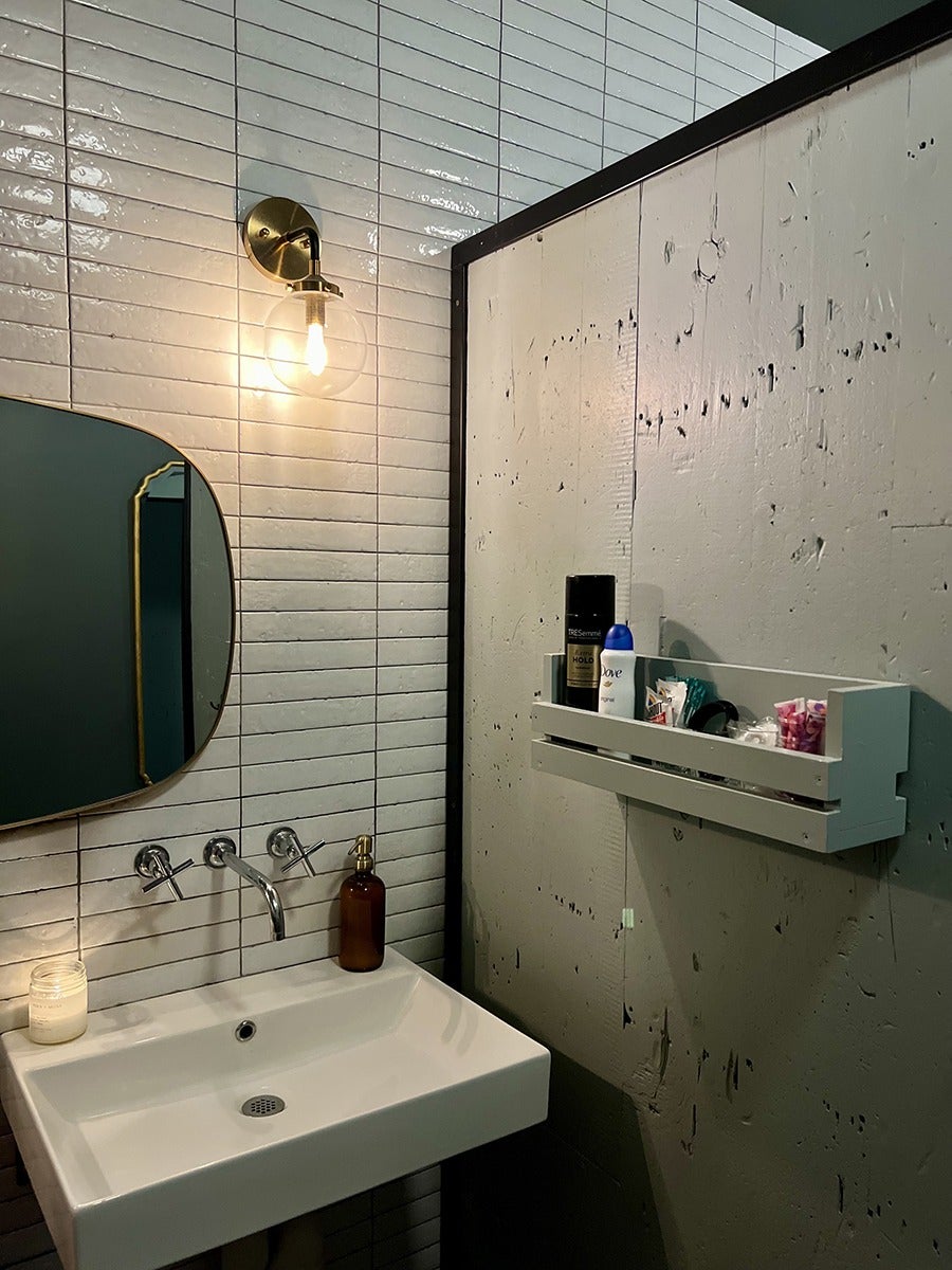 A restaurant bathroom features white subway tiling and a big oval mirror with a thin brass frame.
