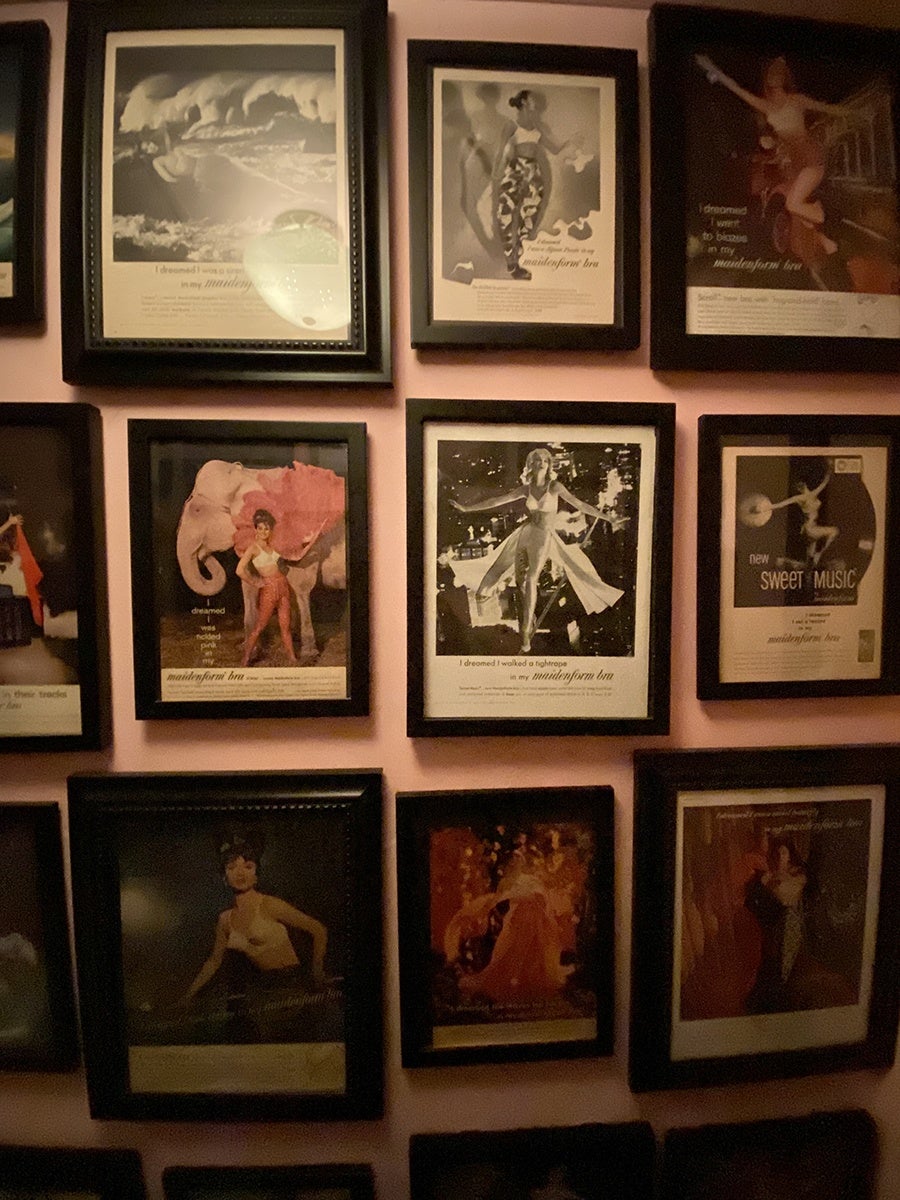 Framed bra advertisements from the mid-1900s decorate a pale pink wall.