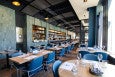 A restaurant interior features green-blue tiling, blue seats, and light wooden tables.