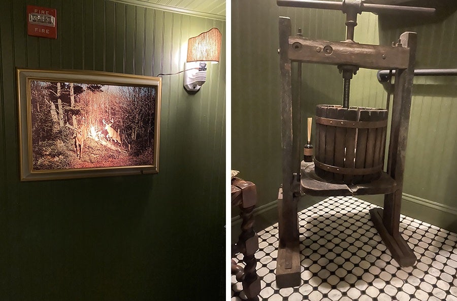 Side-by-side photos show a restaurant bathroom with forest green walls, a framed photo of deer, and an old wooden wine press on a black-and-white tiled floor.