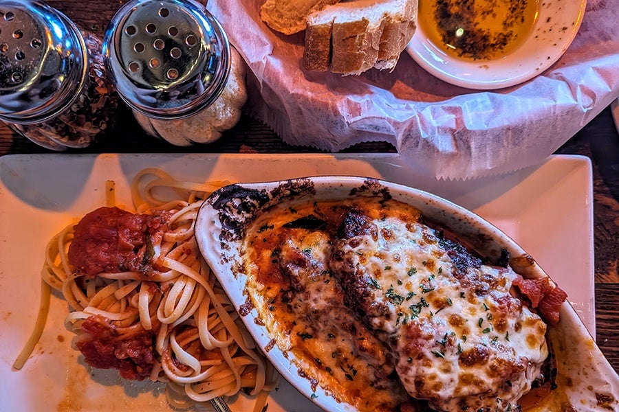 Overhead view of a big piece of chicken parm with linguine and white bread.
