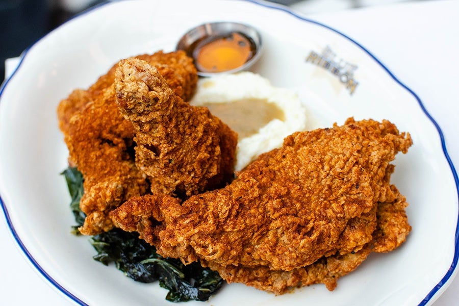 A plate of crispy fried chicken with sides of mashed potatoes and gravy, honey, and cooked greens.