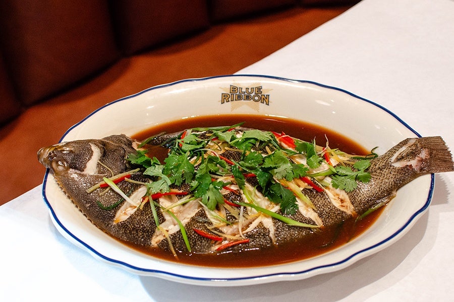 a whole fish is covered in herbs and spices, sitting in a pool of brown sauce.