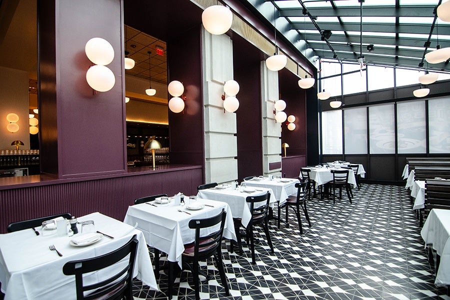 An enclosed patio-like space at a restaurant has a black and white tiled floor and white tablecloth-covered tables.