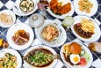 An overhead view of around 10 dishes of food, including steak frites, a burger, a whole fish, fried chicken, and more.