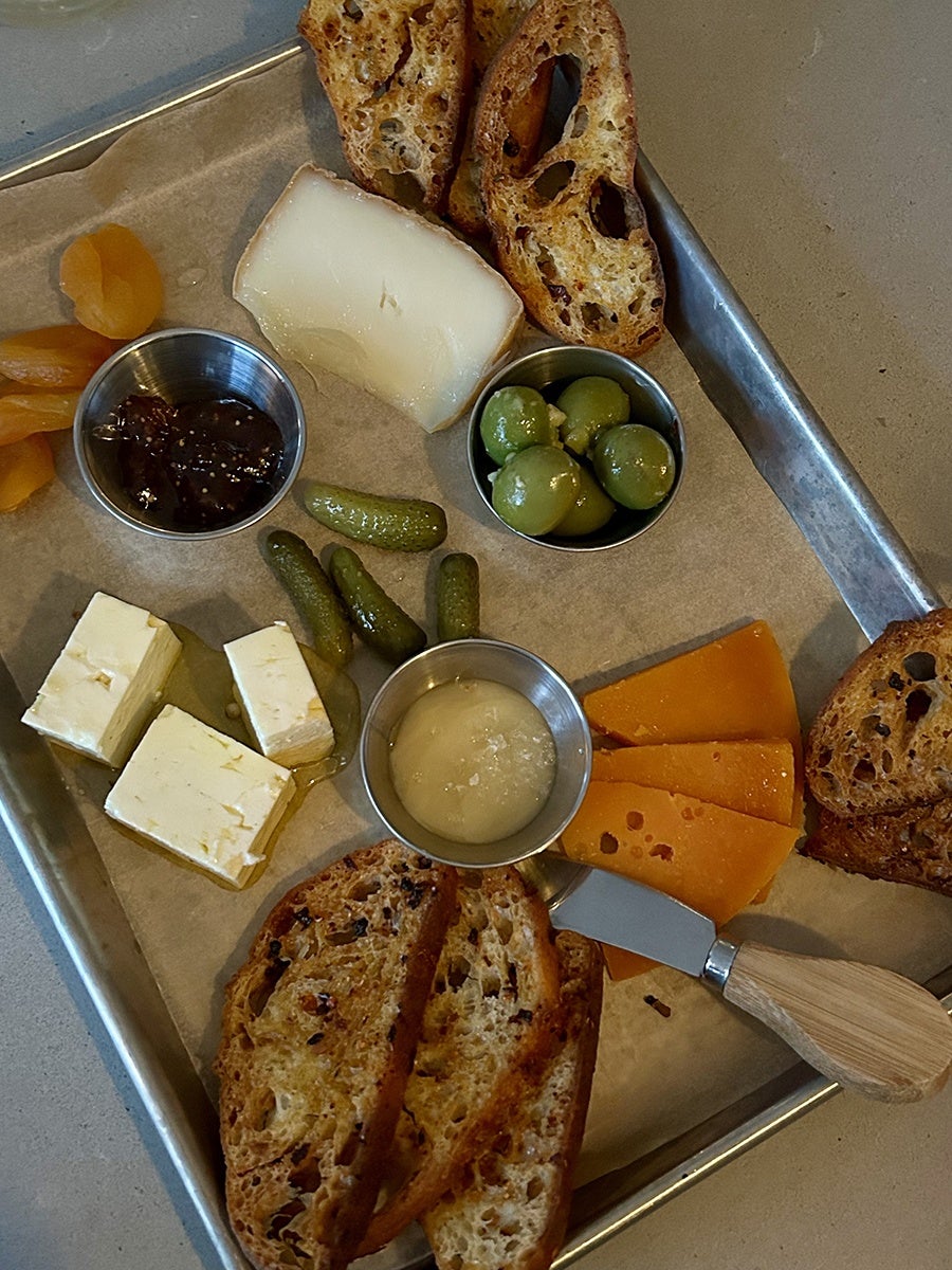 Overhead view of a metal tray of cheeses, bread slices, olives, and more.