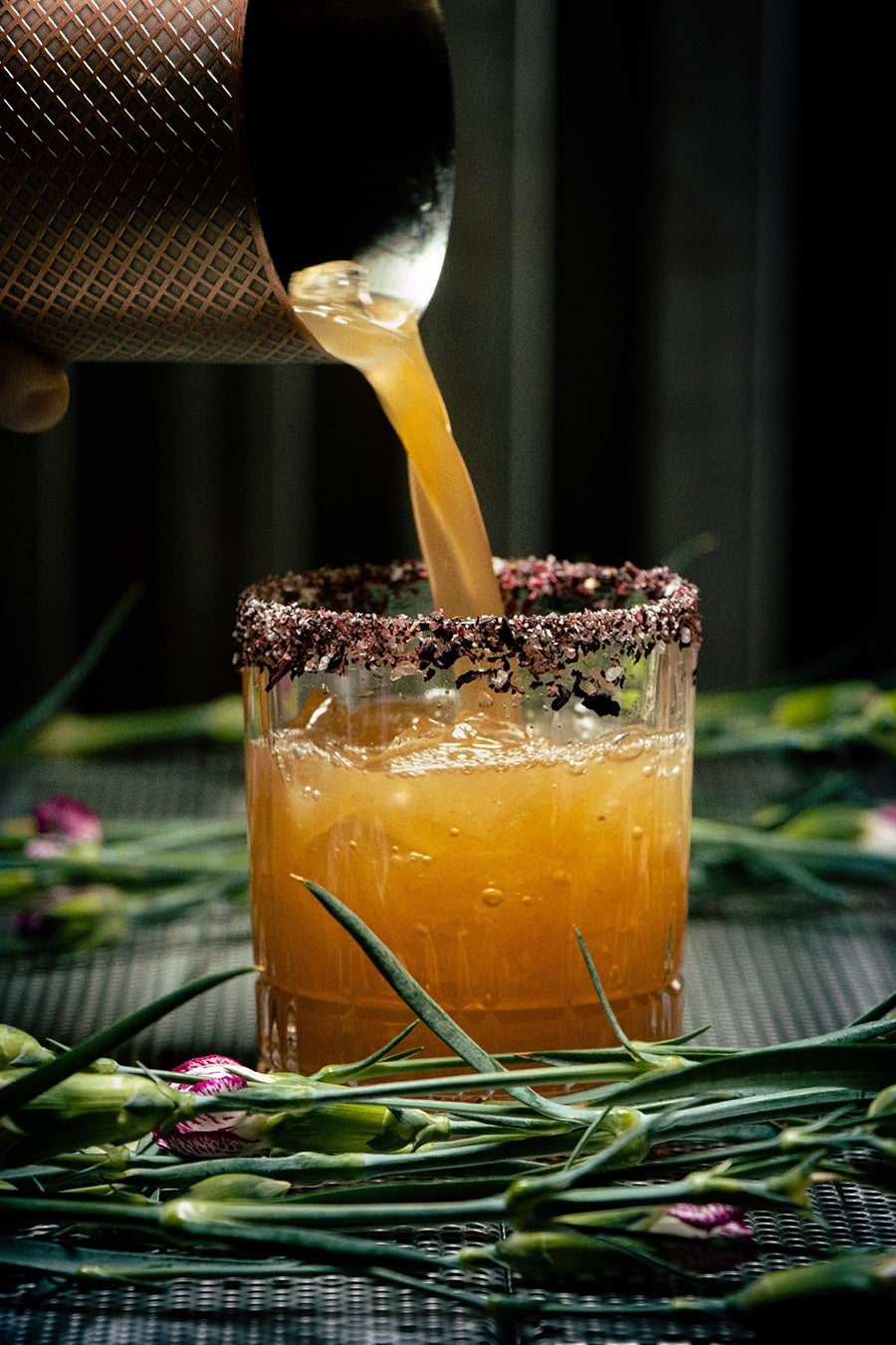 A glass holding an orange cocktail has a black salt rim.