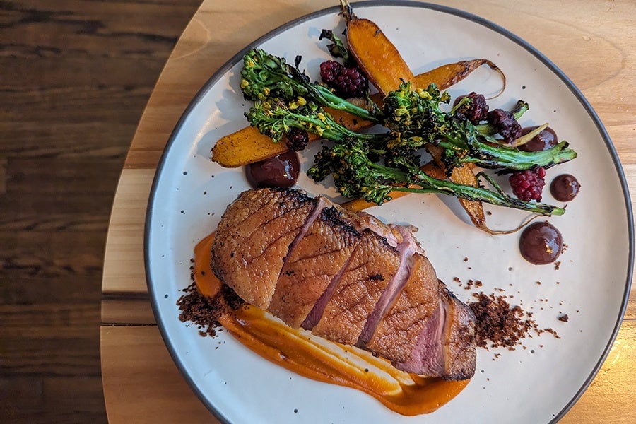 Overhead view of sliced, rare duck breast with roasted carrots and broccolini.