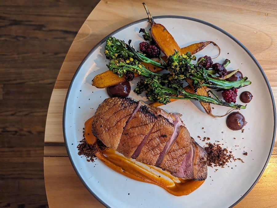 Overhead view of sliced, rare duck breast with roasted carrots and broccolini.