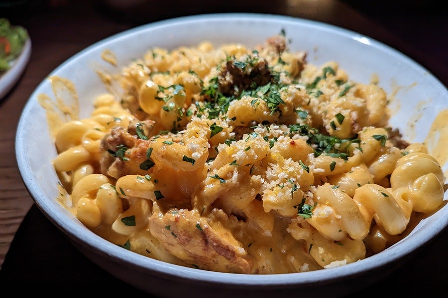 A bowl of mac and cheese, made with cavatappi, has an orange-yellow sauce and chopped herbs as garnish.