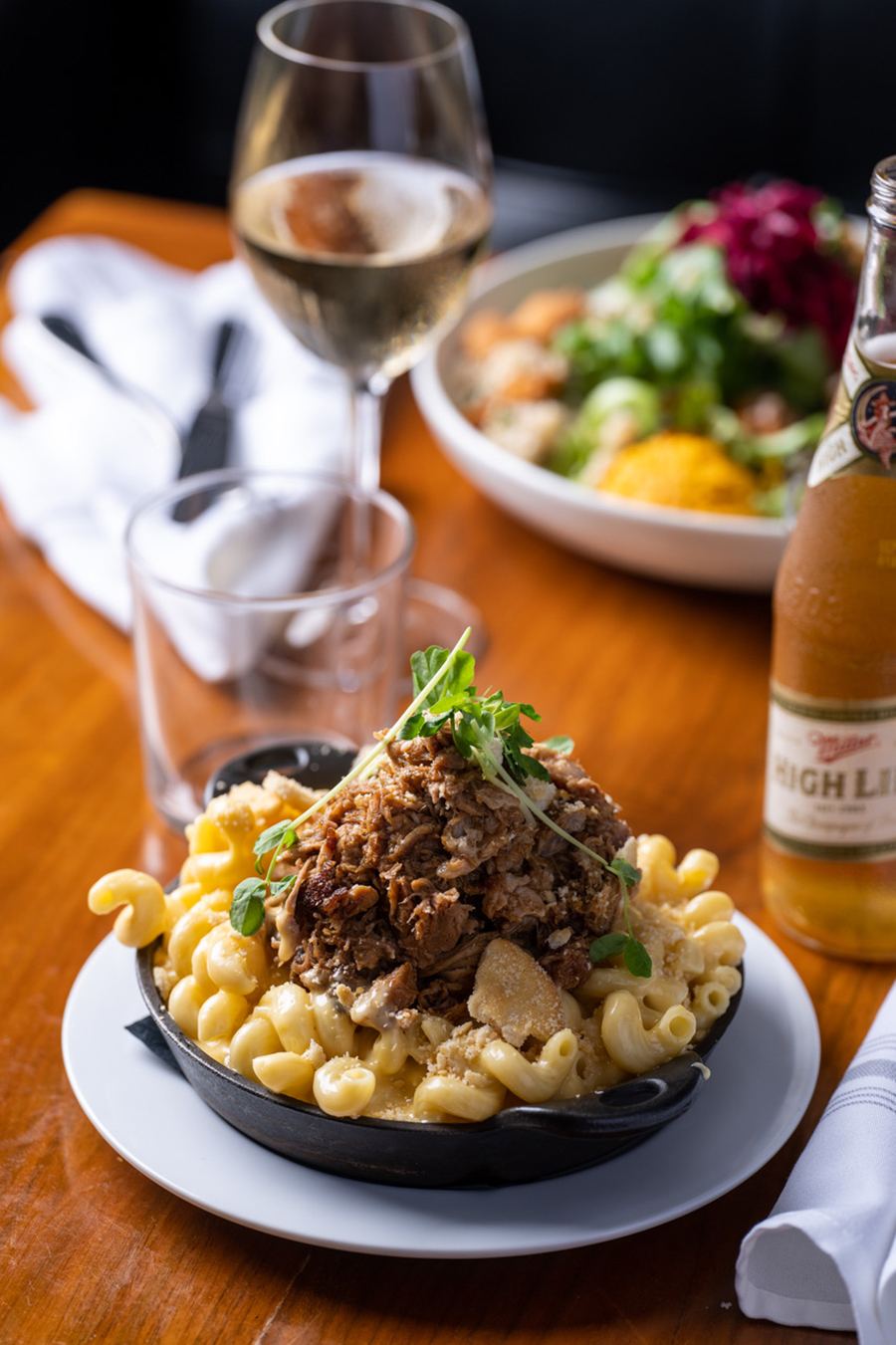 A cast-iron pan of mac and cheese is topped with a pile of pulled pork and some green garnish.