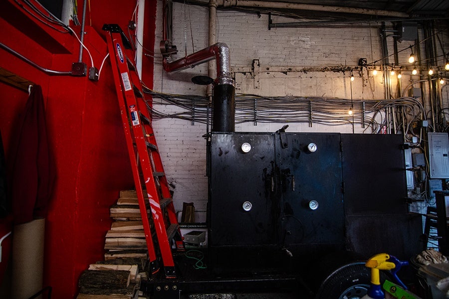 A meat smoker sits inside of a space with a bright red wall and a white brick wall.