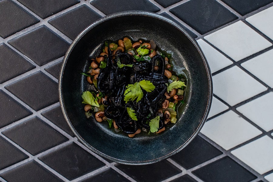 Squid tossed in jet black squid ink sits atop a bed of black-eyed peas in a black plate.