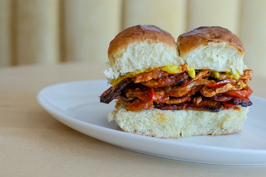 Two small buns sit next to each other, stuffed with grilled pork topped with mustard and peppers.