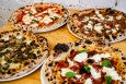 A quartet of leopard-spotted pizzas with various toppings sits on a table.