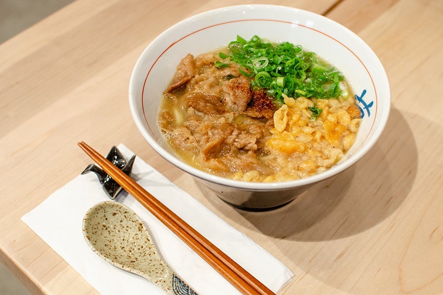 A large bowl of udon topped with beef, scallions, and crispy tempura flakes.