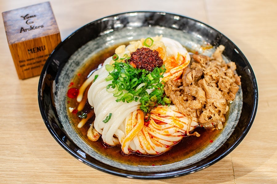 A big pile of udon sits in a cold broth, topped with thinly sliced beef, scallions, and chili oil.