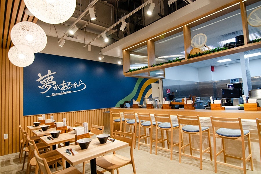 Interior of a small Japanese noodle shop with lots of light wood and an open kitchen.