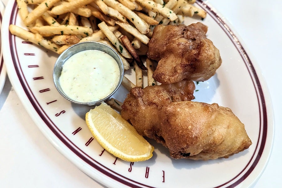 Crispy pieces of whitefish are accompanied by a thick white sauce, a lemon wedge, and thin fries with flecks of herbs.