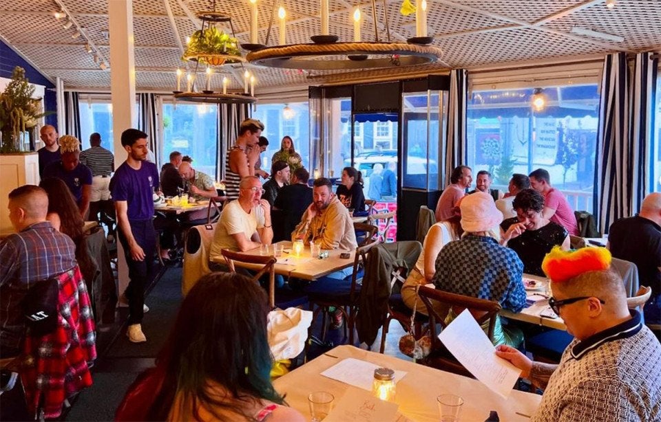 A casual, but stylish dining room with LGBTQ+-friendly patrons with pegboard-like ceilings and lighting fixes of electric-candles and rope.