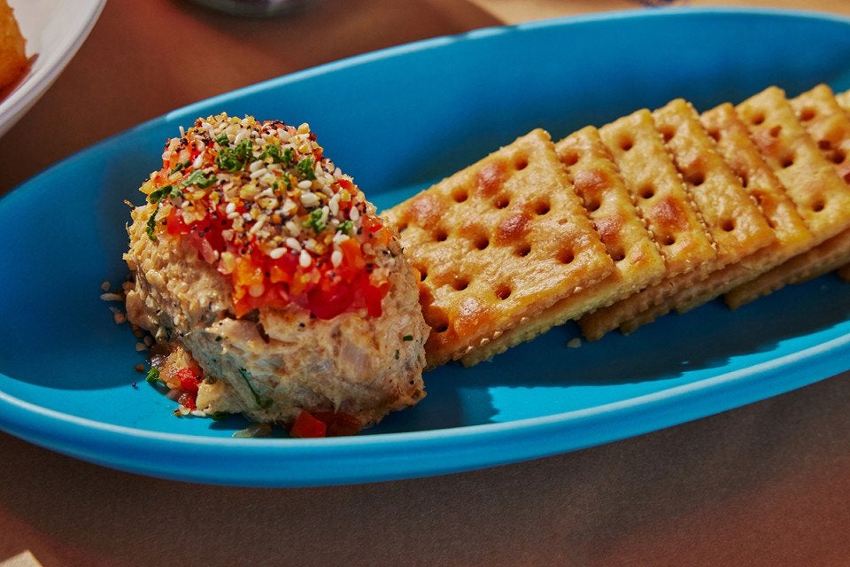 A large dollop of pimento cheese beside a row of grilled Saltine crackers, all served on a light blue oval plate.