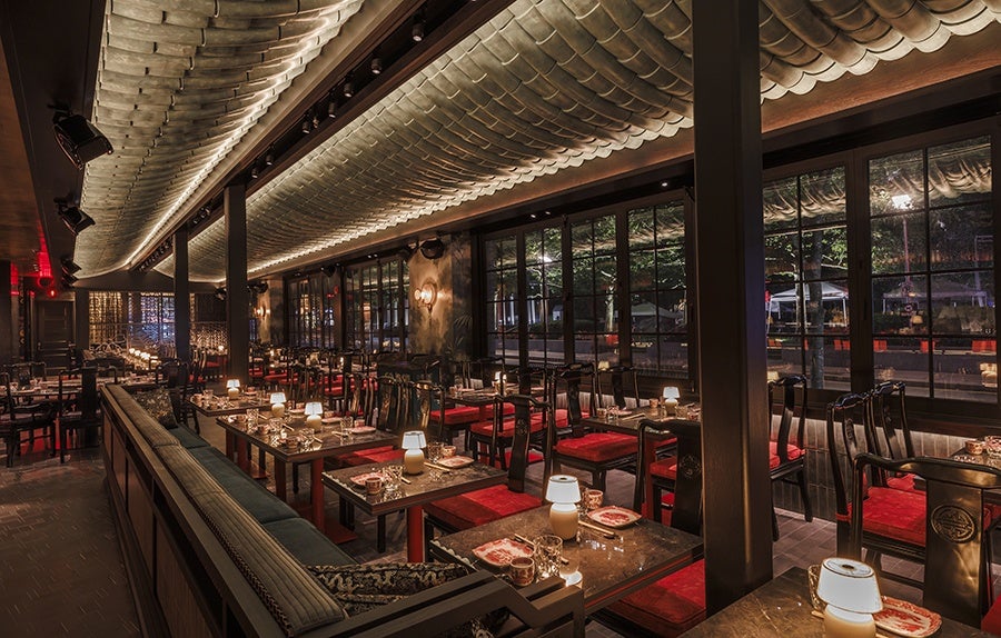 A dimly lit restaurant dining room features black and red tones and swanky vibes.