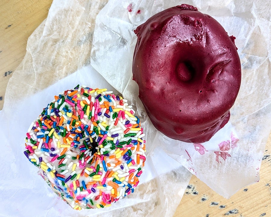 Overhead view of two doughnuts, one covered with vanilla icing and rainbow sprinkles and the other covered with a dark pink glaze.