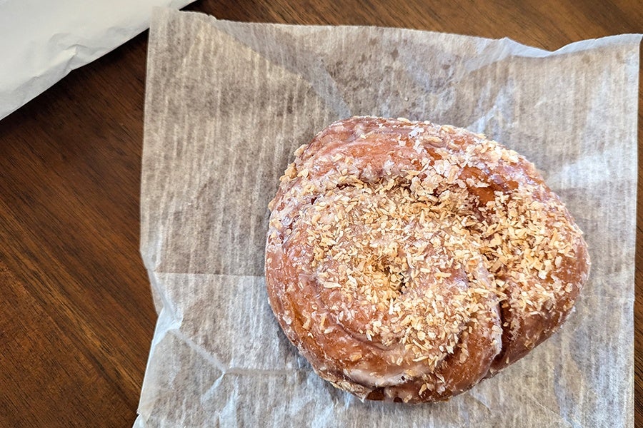 Overhead view of a glazed, buttercrunch-topped swirl-shaped coffee roll on tissue paper.