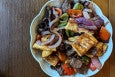 Overhead view of a stir-fried dish of lamb strips, chunks of flatbread, red onions, and bell peppers.