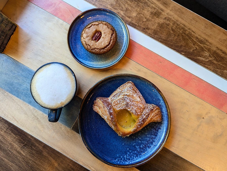 Overhead view of two pastries and a cappuccino on a wooden table with colorful painted stripes.