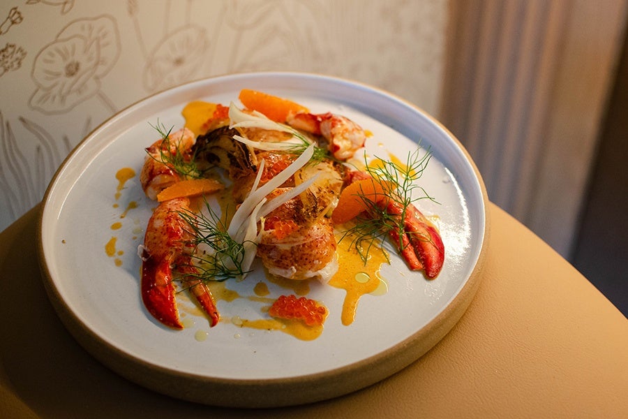 Cooked lobster is served with citrus slices and a drizzle of orange sauce.