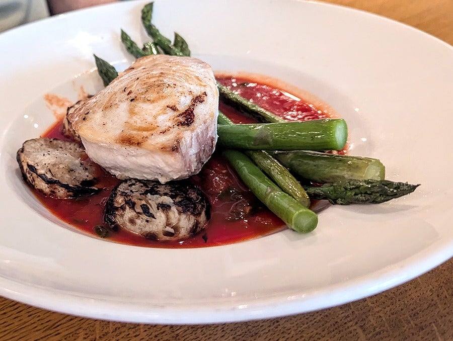 Closeup of a seared fish filet with asparagus and roasted turnips in a bright red broth.