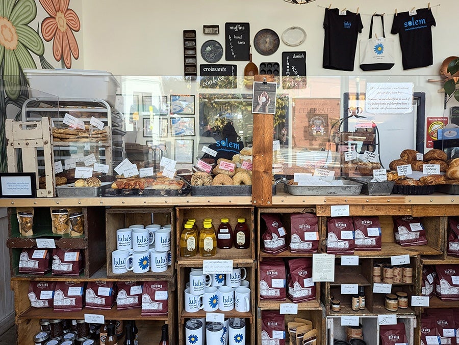 Interior of a bakery, with pantry provisions lining shelfs below a display of baked goods.