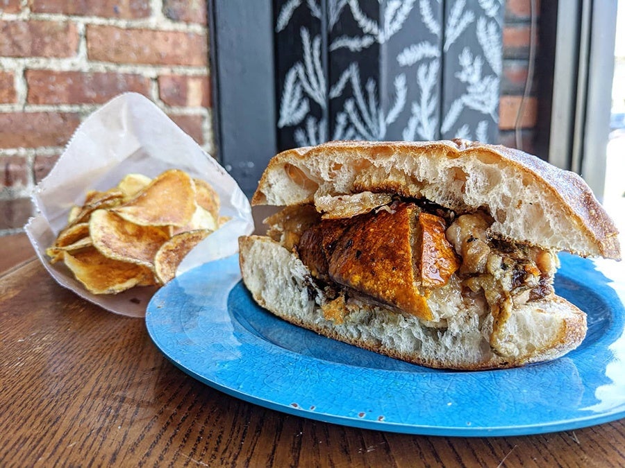 A sandwich features crispy-skin porchetta on crispy bread, with a side of chips.
