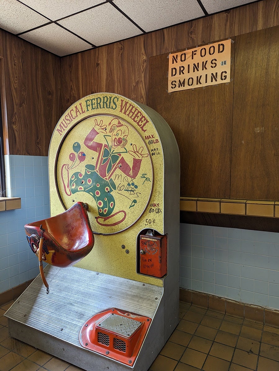 An old-timey carnival ride with a clown is in a room with wooden walls.
