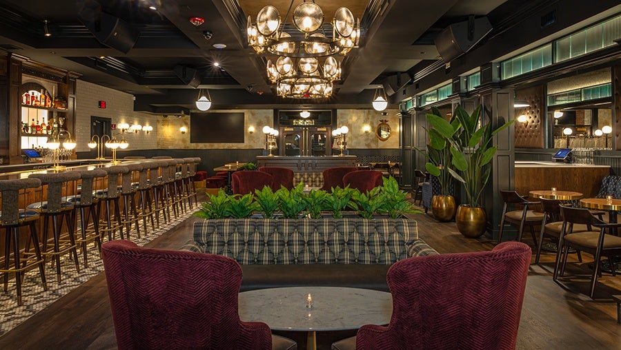 Empty restaurant interior with red velvet armchairs, khaki and gray banquettes, and a long bar.