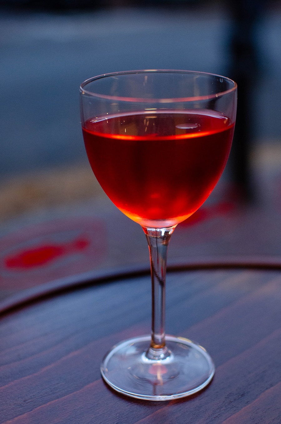 A pinkish-red cocktail is served in a Nick and Nora glass.