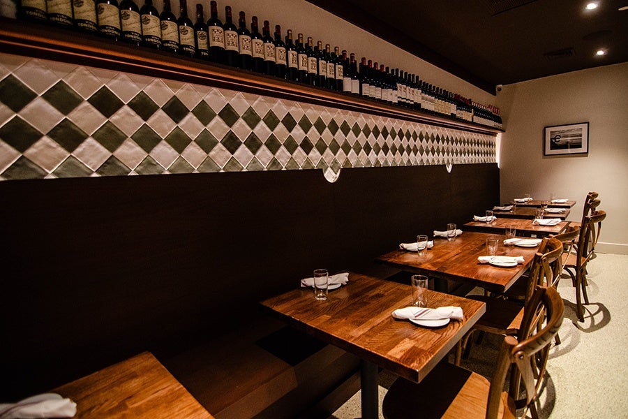 A restaurant dining room features a wall of green and white alternating diamond tiles and glossy wooden tables.