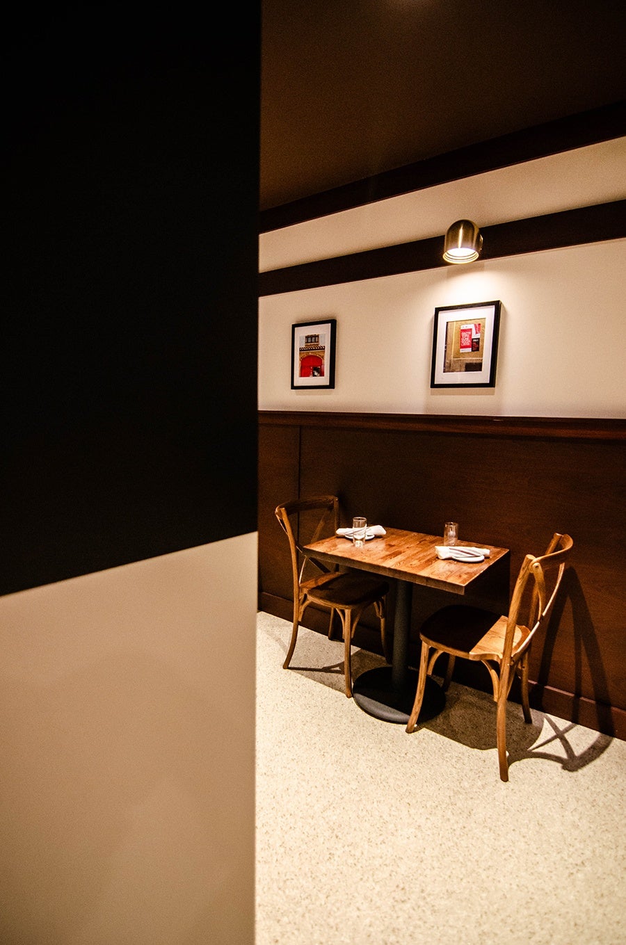 A wooden table and chairs sits in a restaurant dining room under a photograph of a street scene from Spain.